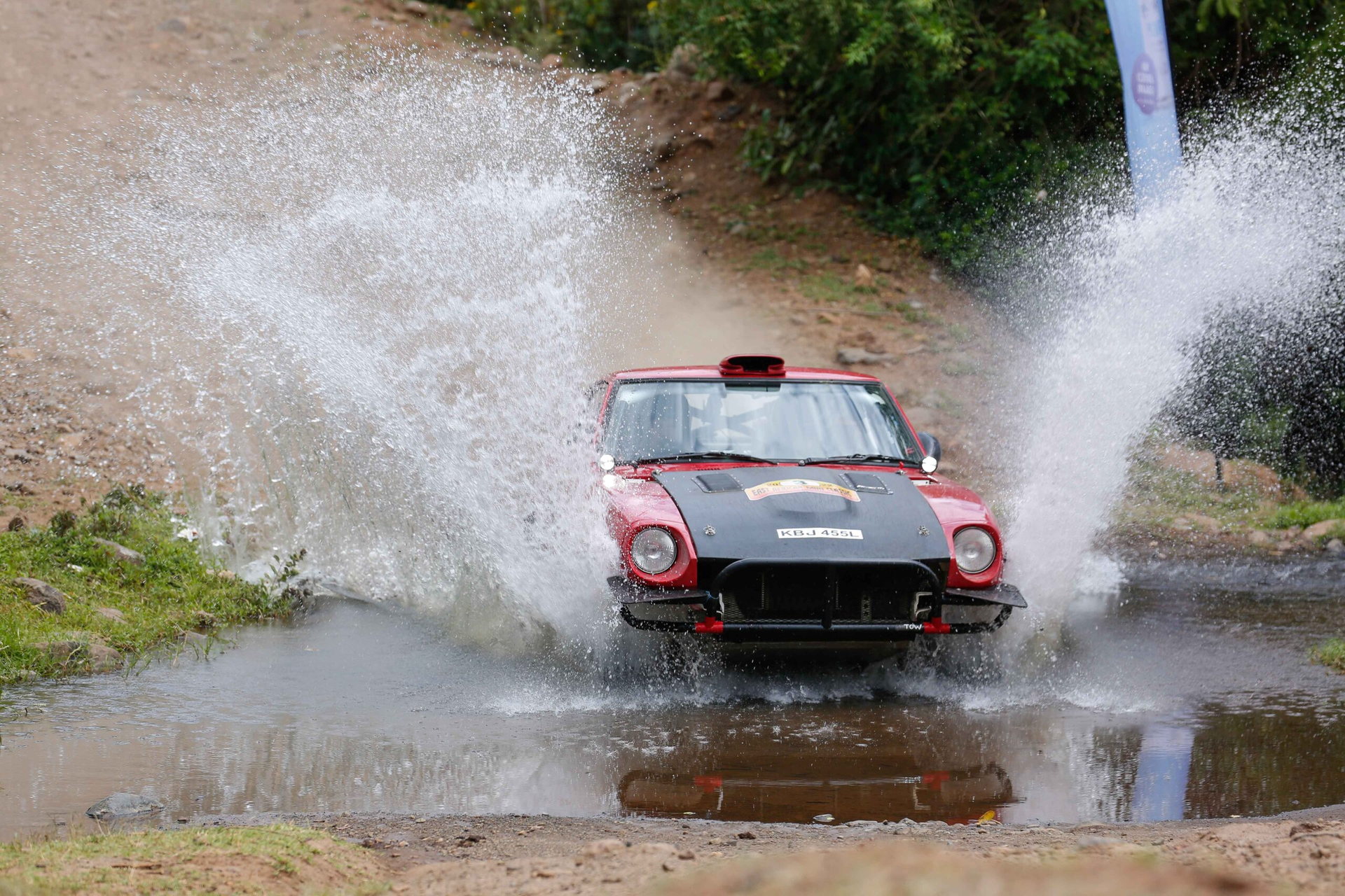 A rally car crossing a shallow stream during an automotive event